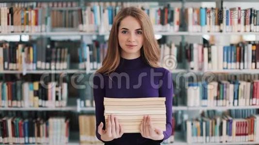 微笑的女学生拿着书站在图书馆的书架前视频