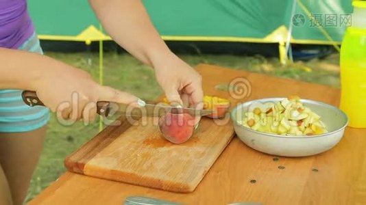 一个年轻的女人用刀把一个桃子从石头上洗掉。视频