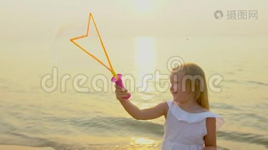 快乐可爱的小女孩在美丽的夕阳下，在海滩上玩肥皂泡，在缓慢的假期里快乐的度假视频