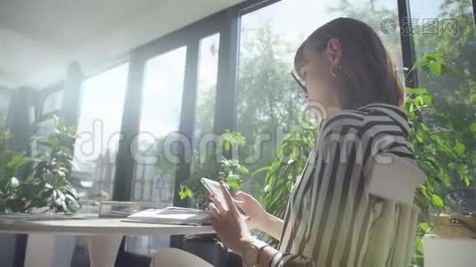 Brunette女士独自一人在一家有全景窗户的咖啡馆里，使用智能手机视频
