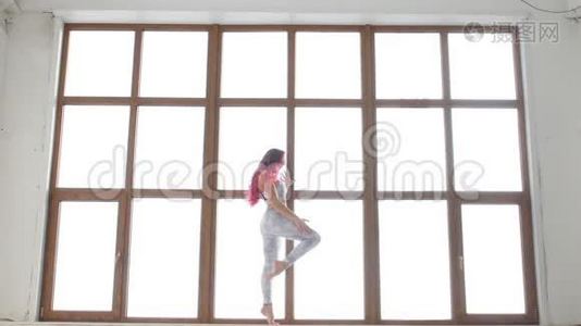 拉伸和柔韧性的概念.. 穿着运动服的年轻女子在白色的室内靠近窗户伸展身体视频