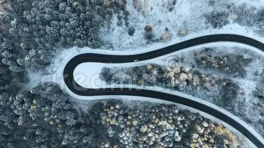 头顶高空俯视汽车行驶在簪弯转弯的山路上，冬雪覆盖森林。 白色视频