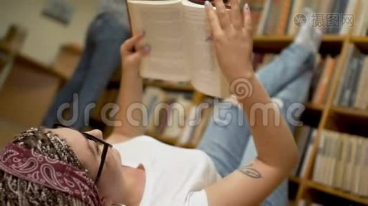 漂亮的女孩正在图书馆的地板上读一本书。视频