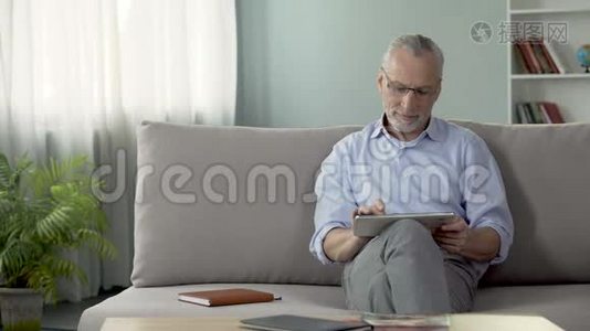 微笑的老人坐在沙发上，看女儿的平板照片视频