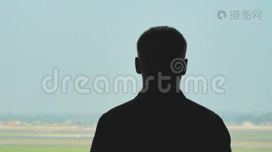 一个年轻人看着飞机在蓝天上起飞的剪影。视频