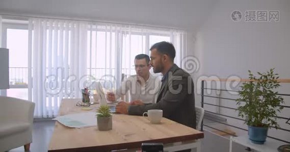 两个成年白种人商人使用笔记本电脑并在办公室内交谈的肖像视频