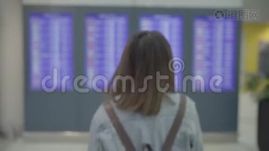 快乐的亚洲女人看着信息板，在登机口的候机大厅里拿着行李检查她的航班。视频