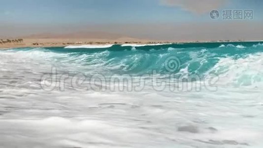 在阳光明媚的日子里，金色沙滩上的蓝色海浪翻滚着4k慢镜头视频
