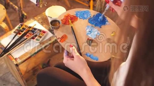女艺术家拿着调色板与蓝色和红色的油彩和绘画图片特写。视频