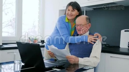 网上购物快乐的老年夫妇用笔记本电脑在线支付，享受商业上的成功，并拥抱在。视频