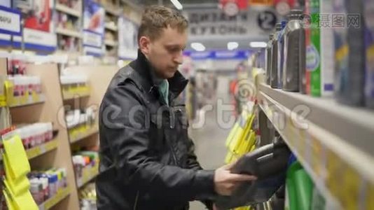 年轻人在维修服务站或超市为汽车选择机油。 货架上有不同的罐子视频