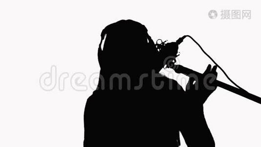 一个年轻女孩在录音室麦克风里唱歌的剪影。 白色背景上的特写。视频