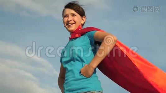 美丽的女孩超级英雄穿着红色斗篷站在田野上，斗篷随风飘扬。 慢动作。 特写镜头。 女孩的梦想视频