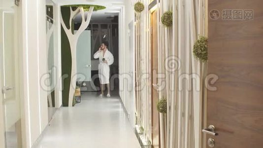 穿着白色长袍的年轻人走在豪华水疗中心的大厅里，用手机交谈。视频