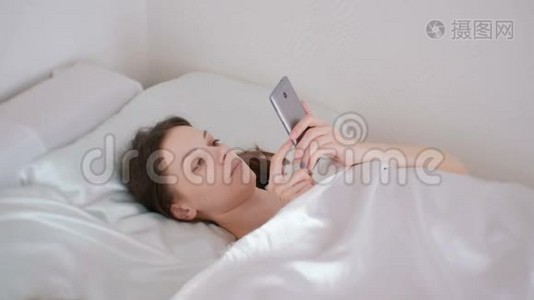 女人早上躺在床上看手机里的东西。视频