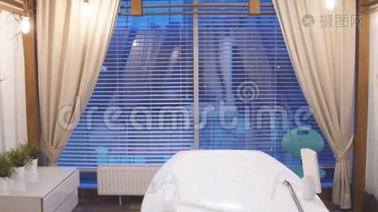 年轻迷人的男子穿着白色长袍休息在豪华水疗中心。 站在全景窗前的男人在一个视频