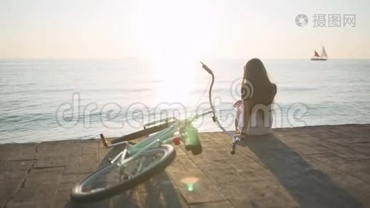 年轻漂亮的长发女人在日落或日出时在海上玩得很开心。 有自行车的女人。 后面的游艇视频
