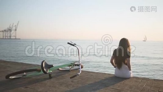 年轻漂亮的长发女人在日落或日出时在海上玩得很开心。 有自行车的女人。 后面的游艇视频