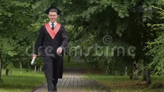 快乐微笑的毕业生带着毕业证书在公园散步，兴奋地跳跃着视频