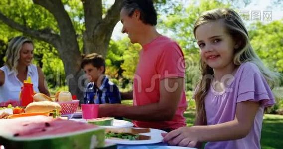 女孩坐在桌子旁，和她的家人在公园4k吃晚饭。视频