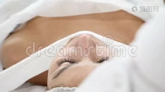 美容诊所。 年轻女人有专业的面部手术。 美容师用毛巾温暖女性客户的脸。视频