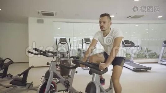 一个人在健身房骑自行车，锻炼他的腿，做有氧训练骑自行车视频