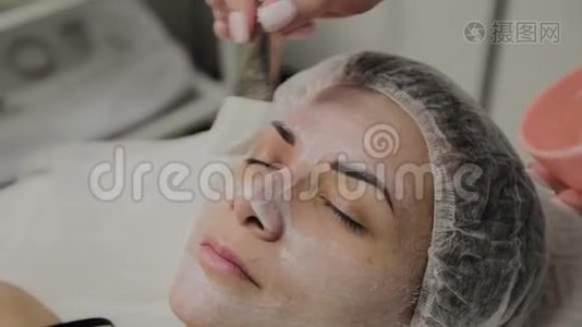 熟练的美容师在室内水疗沙龙里给躺着的女人戴上面具。视频