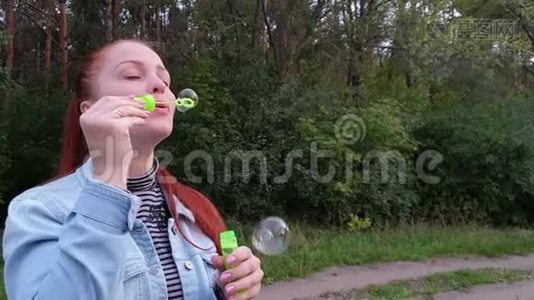 一个夏天的晚上，年轻的女人在公园里吹泡泡。视频