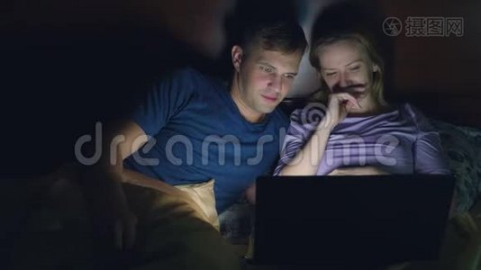 夫妻，男人和女人，在睡觉前在卧室的床上用笔记本电脑看电影。 看喜剧电影，视频