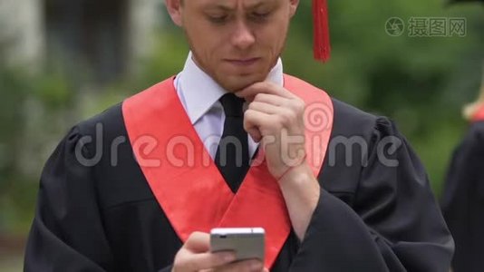 认真的男毕业生揉着下巴，看着智能手机，收到好消息视频