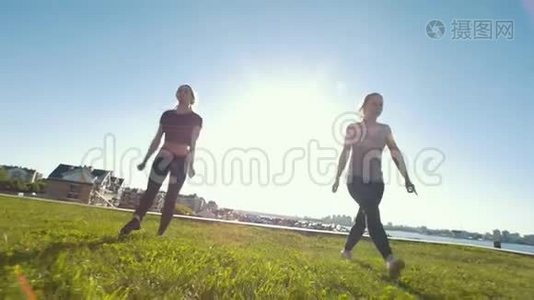 年轻的运动女性在阳光下的草地上表演同步的杂技元素视频
