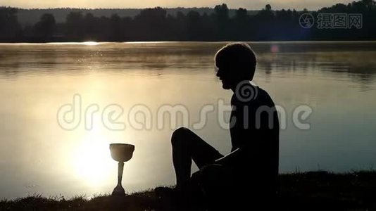 金发碧眼的人坐在湖岸上，看着一只盛满水的冠军碗视频