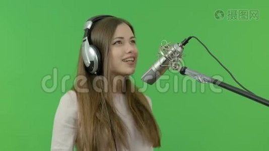 一个年轻女孩正对着录音室的麦克风唱歌。 特写镜头。 在绿色的背景上。视频
