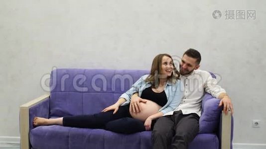 一对已婚夫妇正坐在家里的沙发上等待孩子的出生。 男人抚摸着她的手穿过她视频