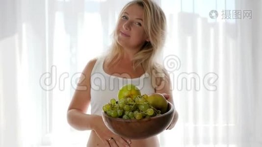裸腹微笑的女人端着新鲜水果的盘子，看着镜头视频