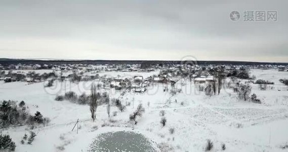 冰冻的池塘覆盖着一场雪和一个村庄附近覆盖着一场雪的植物。 冬季景观。视频