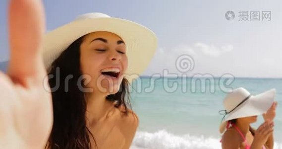 女孩手持手机欢迎女性在沙滩上自拍照，夏日草帽中的快乐游客视频