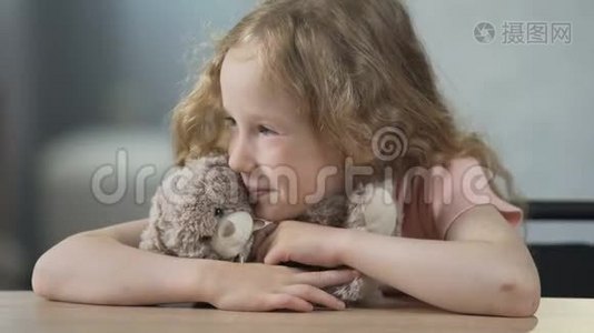 快乐的孩子坐在桌边，抱着泰迪熊，微笑着。 童年视频