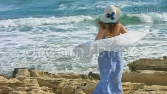 风中挽着围巾的年轻优雅女子，海浪拍打着岩石的海滩视频