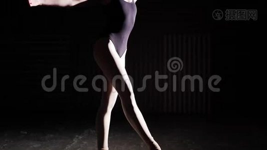 灵活的芭蕾舞演员站在她的尖角芭蕾舞鞋在聚光灯下的黑色背景在工作室。 慢动作。视频