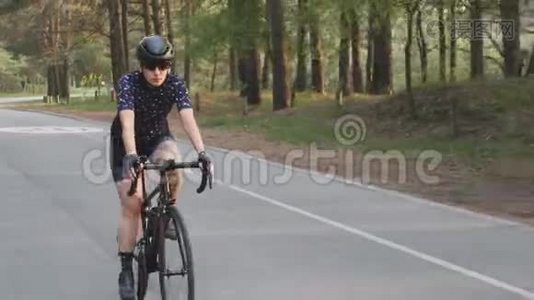 骑着黑色自行车的女孩穿着蓝色球衣和黑色头盔在公园里骑马。 自行车比赛的训练。视频