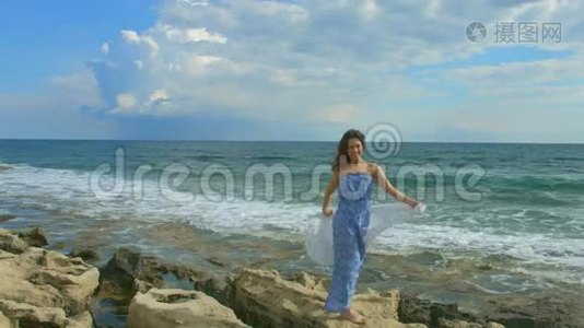 幸福美丽的女人站在岩石般的海滩上，泡沫般的海浪拍打着海岸视频