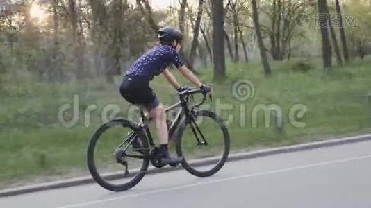 穿着蓝色球衣和黑色头盔的女孩在公园里骑自行车。 公路自行车训练。 自行车的概念。 慢动作视频