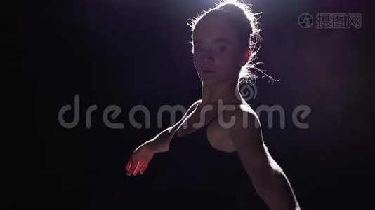 美丽灵活的芭蕾舞演员站在她的尖角芭蕾舞鞋在聚光灯下的黑色背景在工作室。 慢动作视频