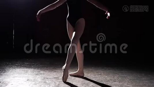 灵活的年轻芭蕾舞演员站在她的尖角芭蕾舞鞋在聚光灯下的黑色背景在工作室。 慢动作。视频