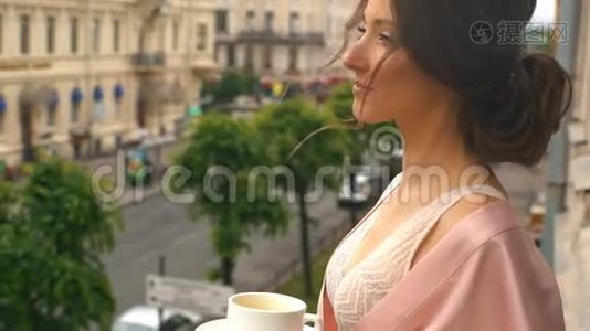 早晨的新娘，一个穿着粉红色丝绸长袍的年轻女子站在阳台上为婚礼做准备视频