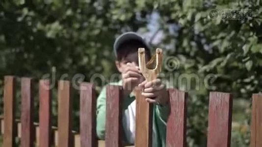 一个带弹弓的滑稽男孩瞄准了村里一个靠近栅栏的人视频