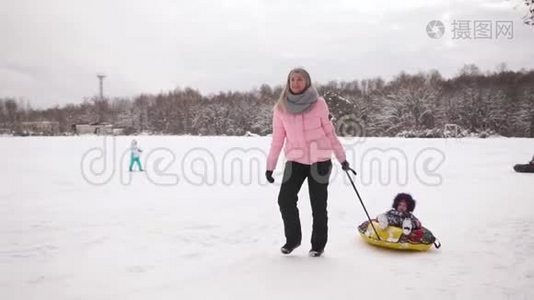 快乐的妈妈和女儿在冬天的雪中雪橇，玩雪球。 母亲和孩子笑着快乐地滑行视频