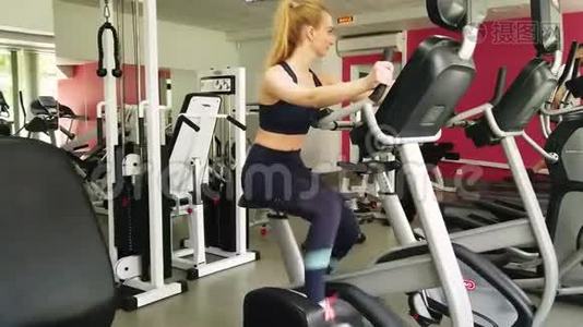 年轻女孩在运动健身房骑着运动自行车跑步。视频