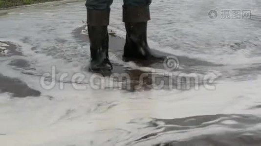 灾难。 村庄里的洪水。 肮脏的黑色河流沿着道路流动。 穿着黑色橡胶靴的人穿过视频